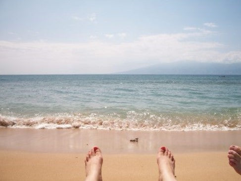 Feet with toenails painted red at a Hawaiian beach with small waves rolling towards them.