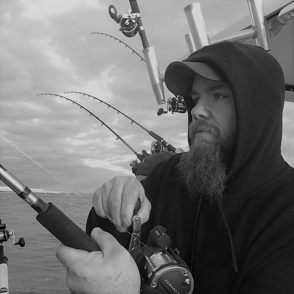 Close up black and white picture of Bryan Hiller holding a trolling fishing rod and reeling. Bearded man fishing.