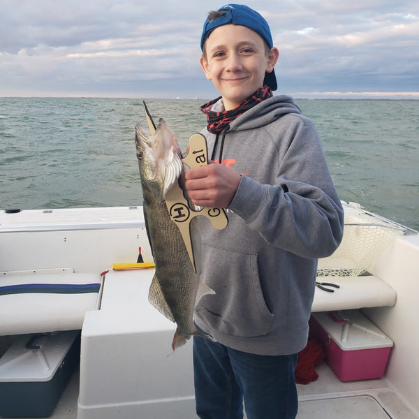 Shane Hiller smiling, holding a walleye from the stern of a charter boat with a fish handling accessory.