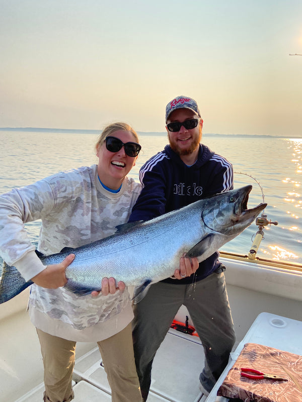 Jennifer Hiller and Michael Hiller both smiling and holding a giant king salmon while standing in a charter boat.