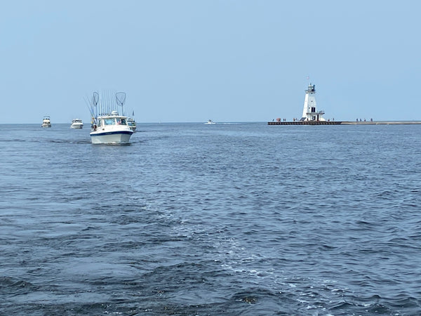 A twenty-five (25) foot Cherokee sportfishing boat with fishing nets and fishing poles in the air next to the Pere Marquette lighthouse in Ludington Michigan 