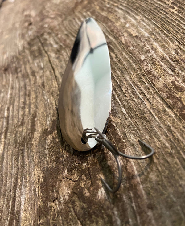 A feather bass fishing spoon with a treble hook attached with a split-ring, laying flat on a plank of grey and brown weathered wood.