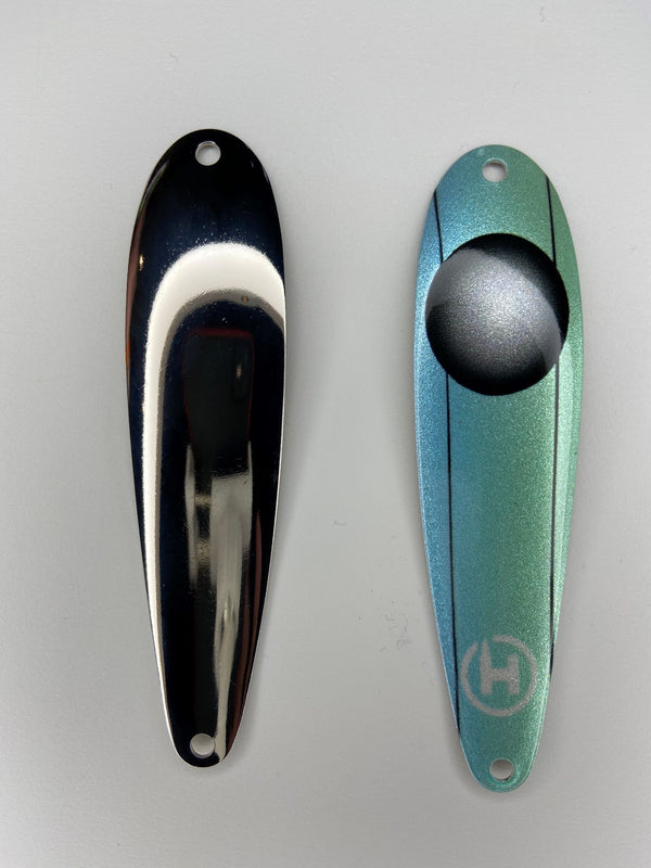 A trolling spoon for lake trout. A light blue and teal lake trout fishing lure with a large black circle near the top, that fades to a white sparkling center.