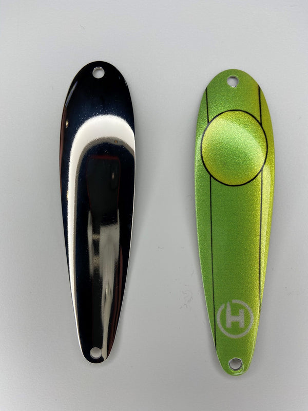 Two fishing lures. A custom brown trout fishing spoon that is lime green and chartreuse with a small, white HangryBrand logo near the bottom. On the lure are thin, black lines that run down its length. Also, an outline of a large circle. Another fishing spoon that is smooth and shiny for brown trout fishing.