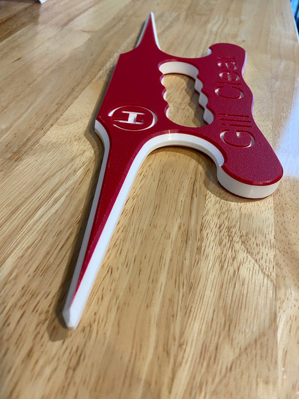 A red and white fish handling device shaped like an anvil sitting on a wooden desk.