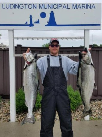 Michael Hiller holding two Salmon and wearing fishing bibs. Man holding salmon caught in Ludington, Michigan.