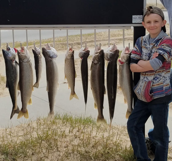 Shane O'Hara Hiller as a pre-teen standing by a King salmon, a Brown trout, and Lake trout he caught.. Boy with arms crossed standing next to many fish.