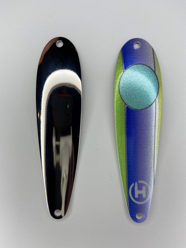 There are two fishing lures. On the right there is a bass fishing lure with a Royal blue stripe down the center and lime green on the left and right sides. This spoon has a turquoise circle near the top with a small white HangryBrand logo near the bottom. On the left there is another fishing lure. The second lure has a smooth, nickel-plated finish.