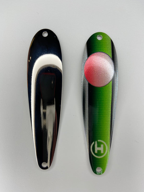There are two fishing lures. On the right there is a bass fishing lure with a Green stripe that fades to black down the center and pearl white and black on the left and right sides. This spoon has a red circle that fades to pearl white near the top with a small white HangryBrand logo near the bottom. On the left there is another fishing lure. The second lure has a smooth, nickel-plated finish.