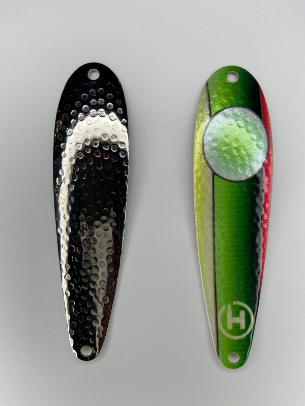 There are two fishing lures. On the right there is a bass fishing lure that is green and yellow on one side and red and black on the other side. This fishing spoon has a pearl white circle that fades to a chartreuse center. It also has a small white HangryBrand logo near the bottom. On the left is the other fishing lure. This one has a hammered style finish and is a bass fishing spoon that is nickel-plated.