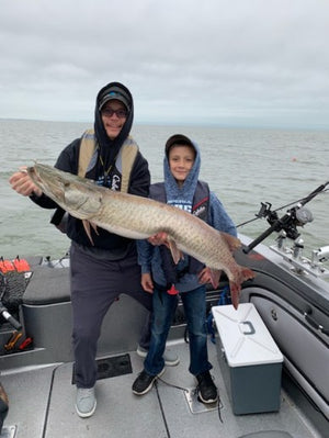 Mike Hiller (left) holding giant Musky along with Shane Hiller (right). Mike Hiller and Shane Hiller standing in a fishing boat and holding a huge Muskie caught on lake St. Clair.